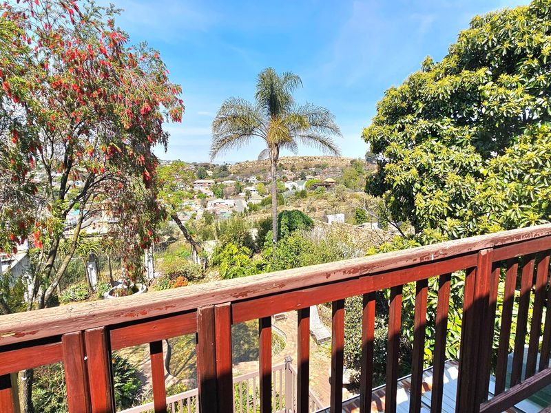 Elevated view overlooking a suburban landscape, framed by a wooden balcony railing and mature garden trees.