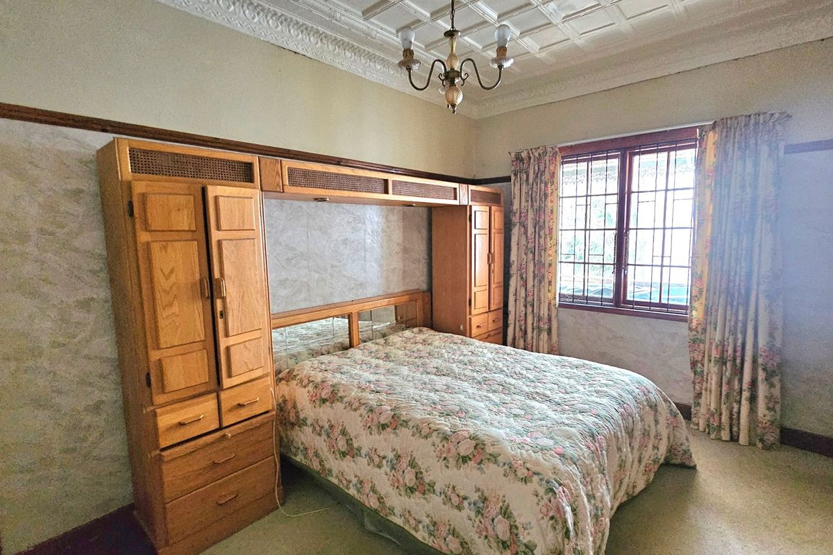 A bedroom featuring a built-in wooden wardrobe unit, ornate ceiling detailing, and security bars on the window.