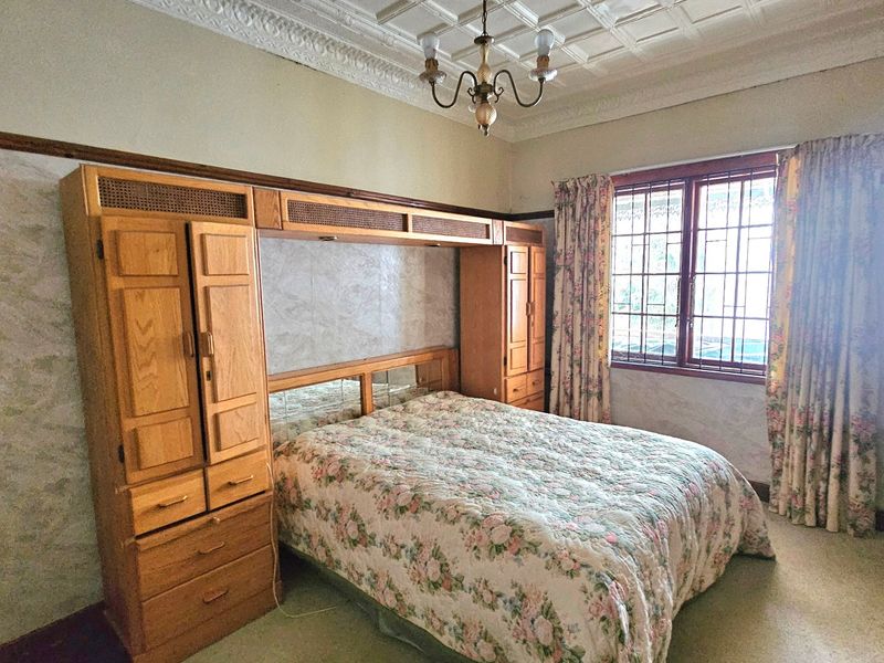 A bedroom featuring a built-in wooden wardrobe unit, ornate ceiling detailing, and security bars on the window.