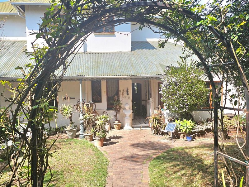 A rear view of the house featuring a covered veranda, a brick paved pathway, and a metal garden arch set within a landscaped garden.