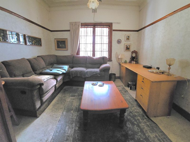 A living room featuring a built-in desk, security bars on the window, and traditional picture rails, offering a functional space with potential for modernization.