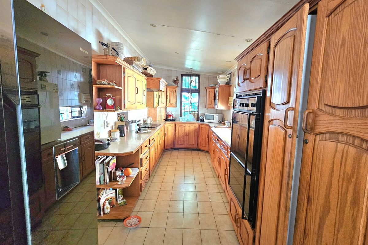A spacious kitchen featuring extensive wooden cabinetry, double wall ovens, tiled backsplash, and ceramic flooring, offering a traditional layout with ample storage space.