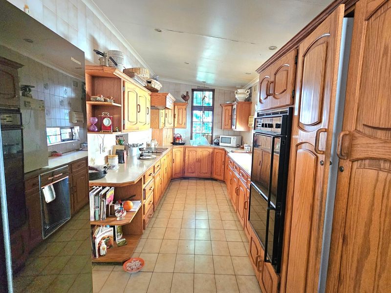 A spacious kitchen featuring extensive wooden cabinetry, double wall ovens, tiled backsplash, and ceramic flooring, offering a traditional layout with ample storage space.