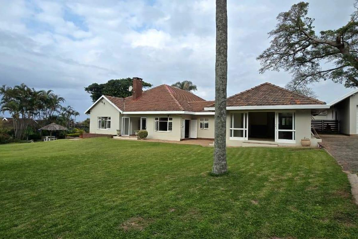 Rear view of the house featuring a spacious lawn, paved patio area, and an attached double garage with a tiled roof.
