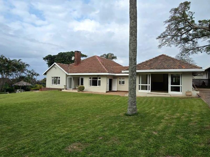 Rear view of the house featuring a spacious lawn, paved patio area, and an attached double garage with a tiled roof.