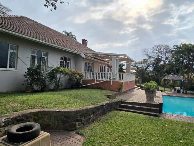 Rear view of the property featuring a swimming pool, covered patio area, and established garden with stone retaining walls.