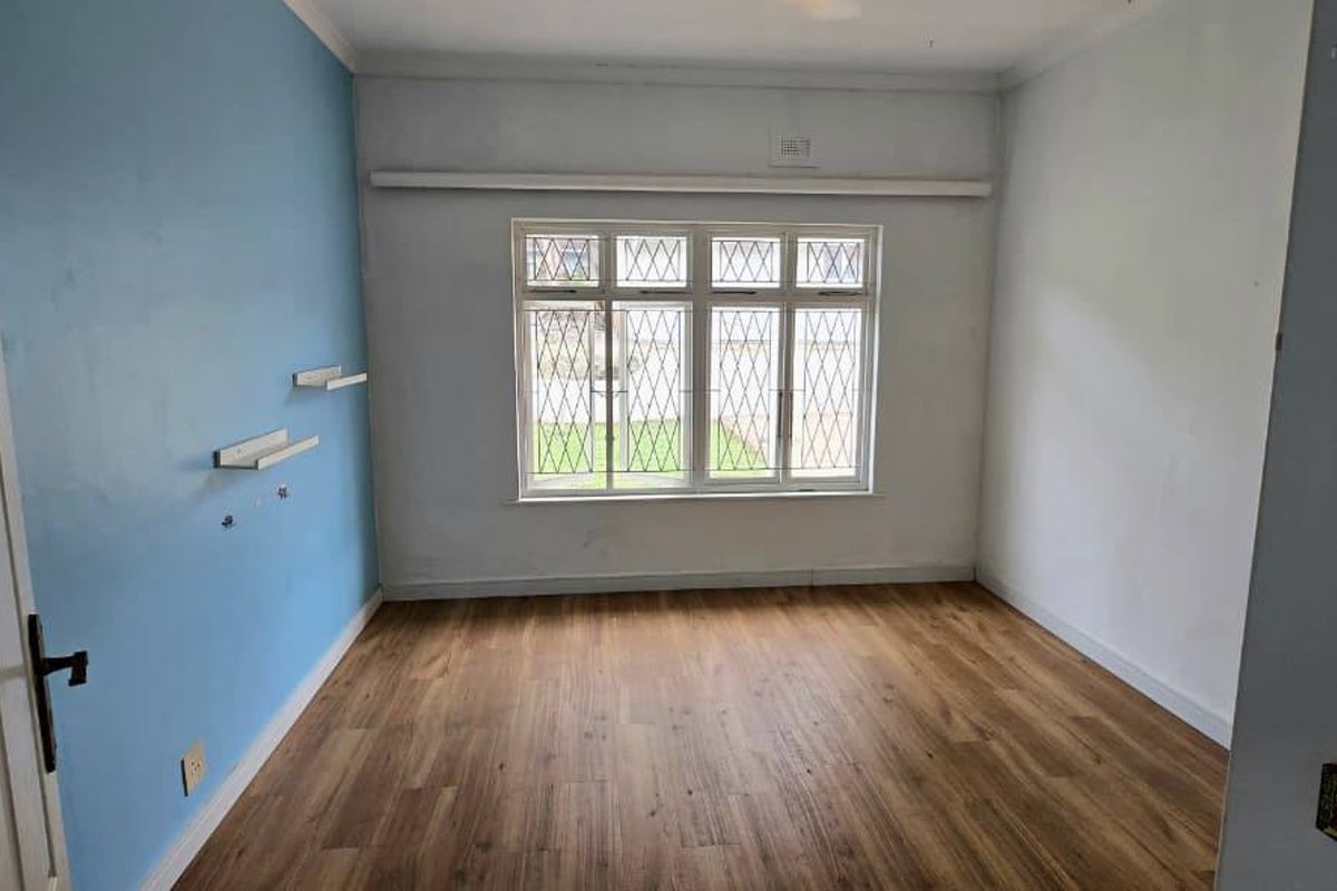 A vacant bedroom featuring laminate flooring, a large leaded glass window with security bars, and a blue accent wall.