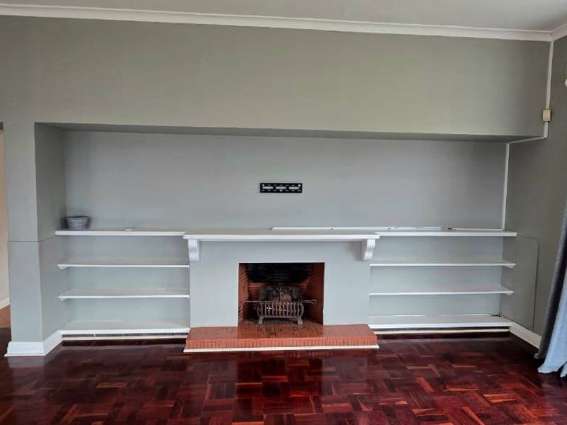 Spacious living room featuring a central fireplace with built-in shelving, classic parquet flooring, and large leaded glass windows overlooking the garden.