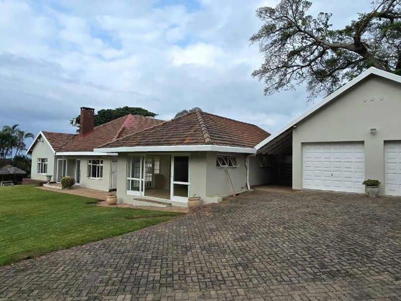 A well-maintained single-story residence featuring a double garage, paved driveway, and a spacious front lawn under a tiled roof.