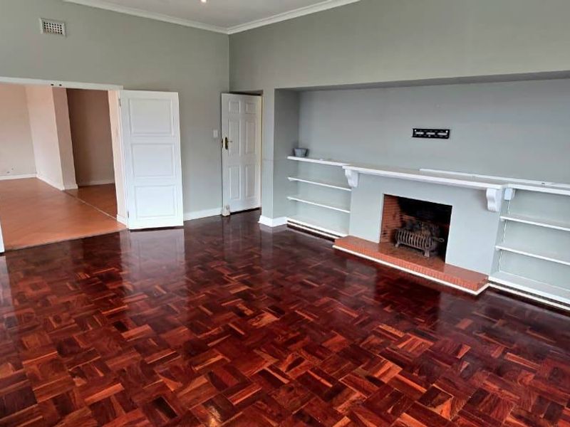 Spacious living room featuring polished parquet flooring, a built-in fireplace with integrated shelving, and double door access to adjacent living areas.