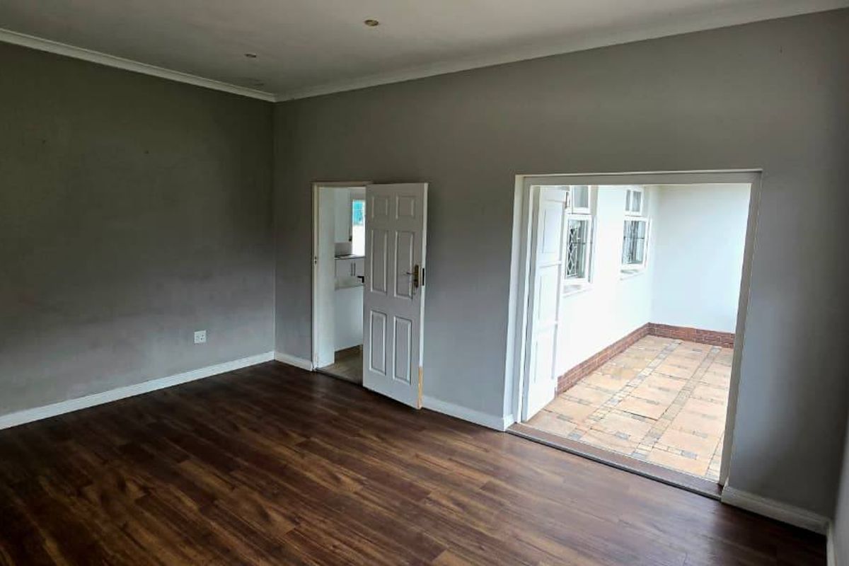 An empty living room featuring laminate flooring, recessed lighting, and direct access to an adjoining tiled patio area through glass-paned doors.