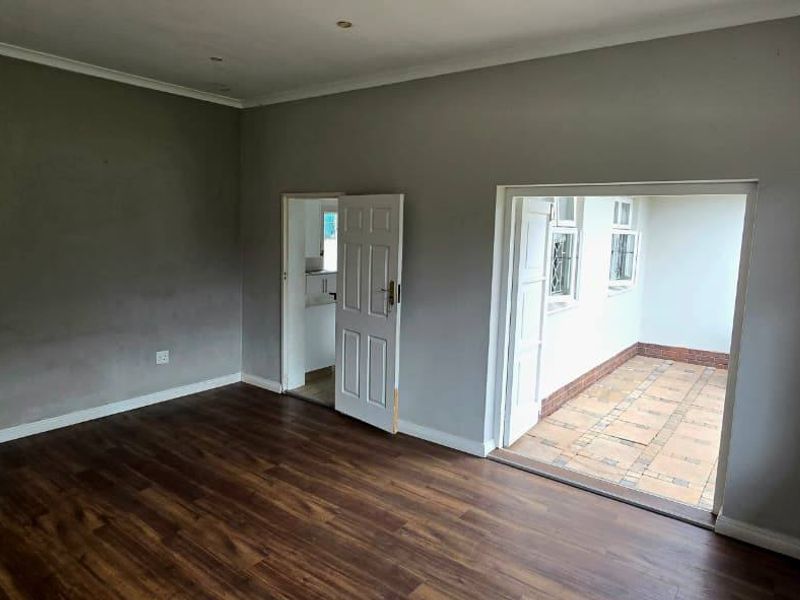 An empty living room featuring laminate flooring, recessed lighting, and direct access to an adjoining tiled patio area through glass-paned doors.