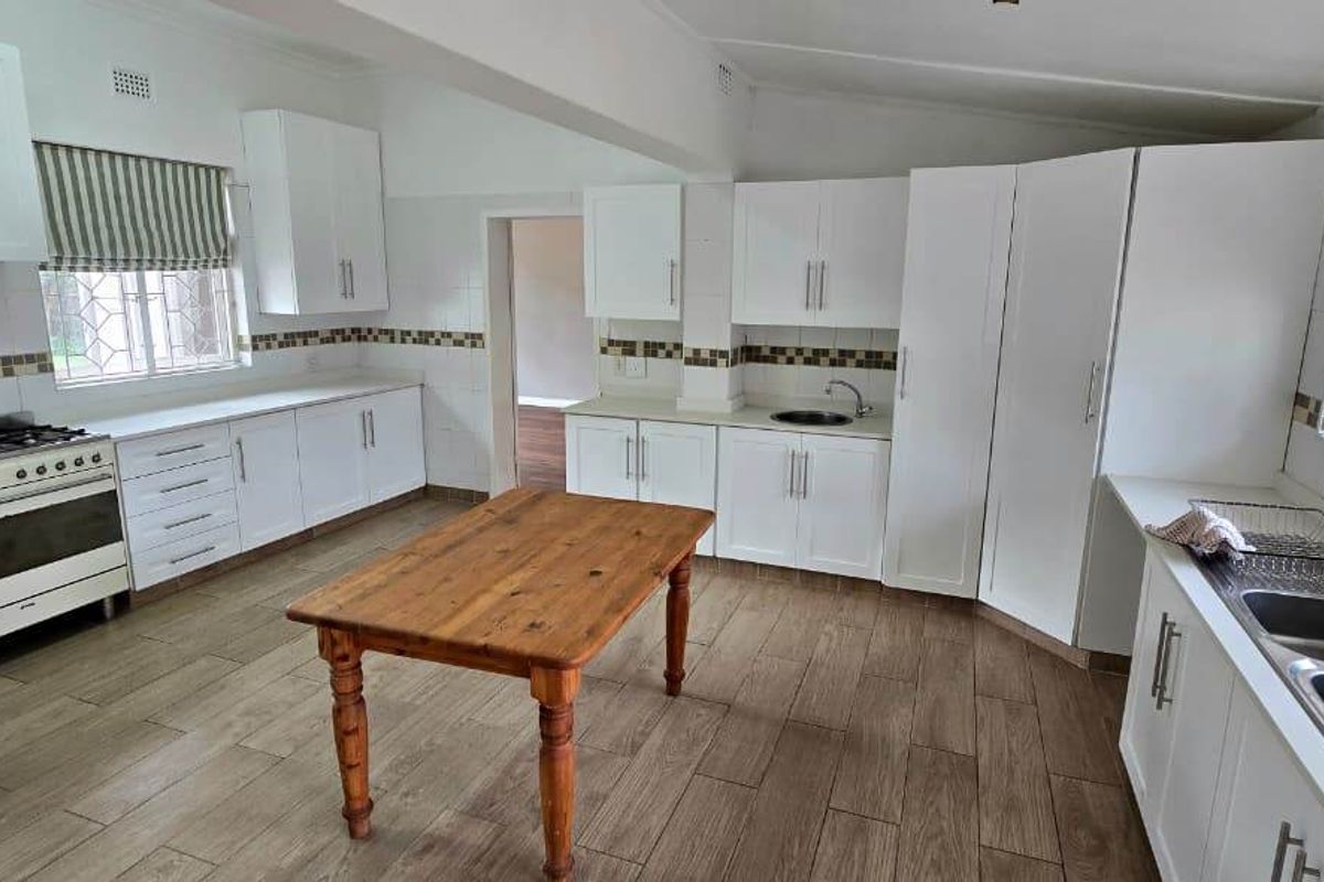 Spacious kitchen featuring white cabinetry, gas stove, double sink, tiled backsplash, and wood-look tiled flooring.