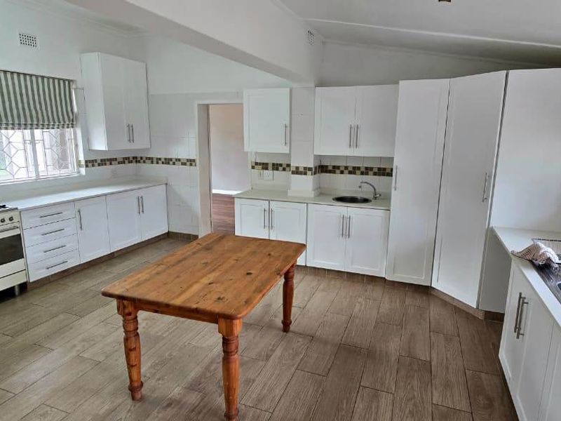 Spacious kitchen featuring white cabinetry, gas stove, double sink, tiled backsplash, and wood-look tiled flooring.