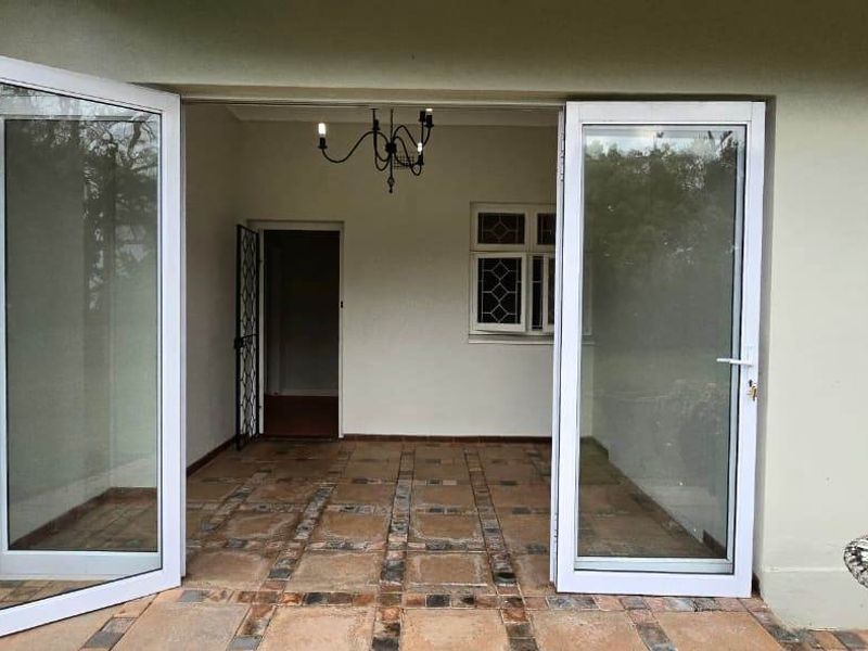 A covered patio area featuring tiled flooring, white aluminium glass doors, and a leaded glass window, providing a transition to the interior living space.