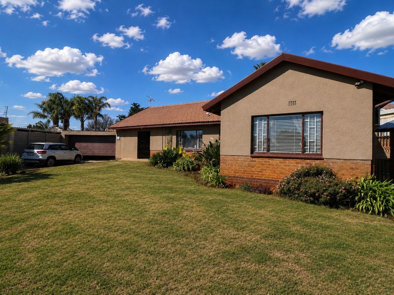 Front view of a single-story house featuring a tiled roof, brick and plastered exterior, and a spacious front lawn with an attached garage.