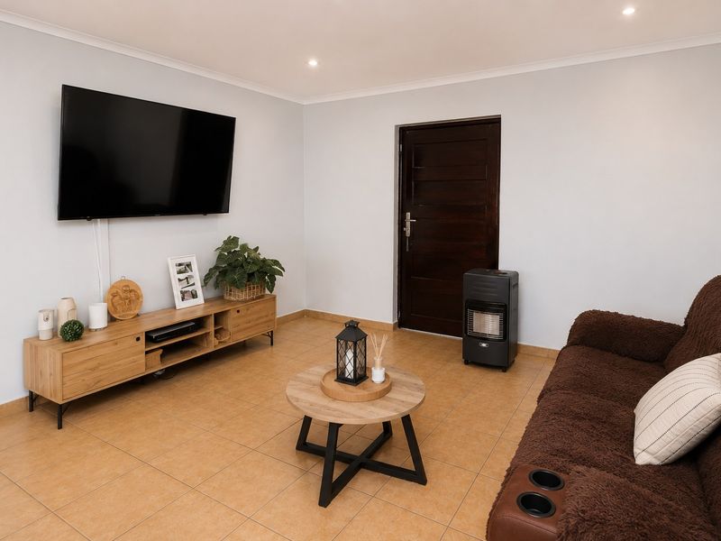A well-maintained living room featuring neutral walls, tiled flooring, recessed downlighting, and a solid timber door.