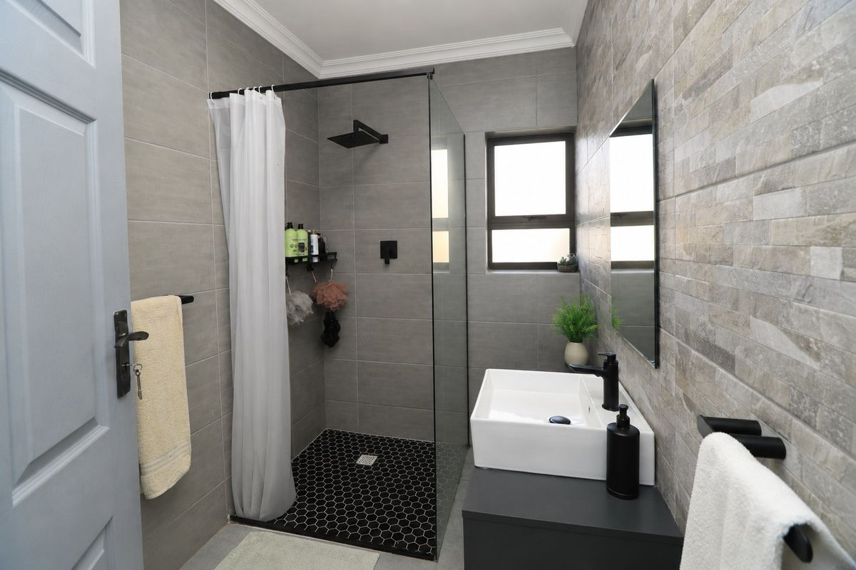 Modern bathroom featuring a walk-in shower with black fixtures, a vessel sink on a vanity cabinet, and stylish grey tiled walls.