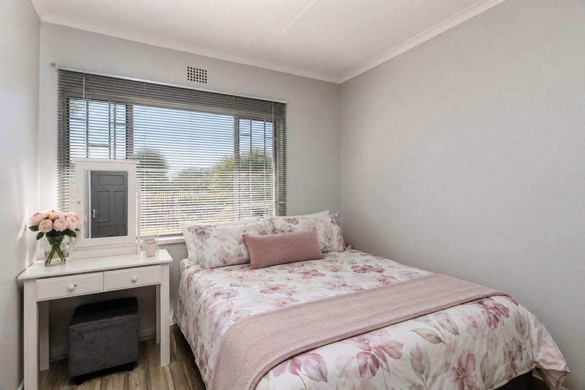 A well-maintained bedroom featuring laminate flooring, neutral wall finishes, and a large window with fitted venetian blinds.