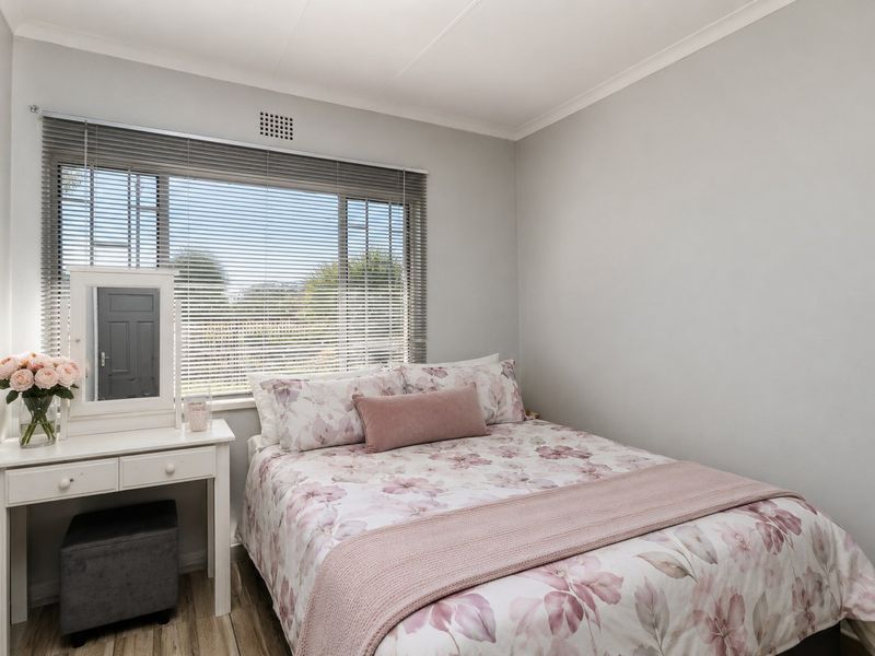 A well-maintained bedroom featuring laminate flooring, neutral wall finishes, and a large window with fitted venetian blinds.