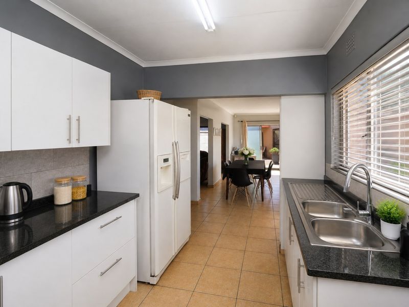 A functional kitchen featuring white cabinetry, dark granite countertops, a double stainless steel sink, and tiled flooring, with an open flow to the dining area.
