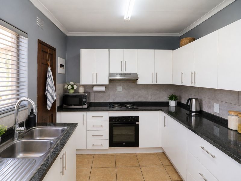 A well-maintained kitchen featuring white cabinetry, granite countertops, a built-in oven and hob, and a stainless steel double sink.