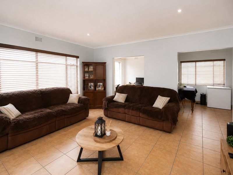 Spacious open-plan living area featuring neutral walls, tiled flooring, and large windows with venetian blinds, offering a bright and functional layout.