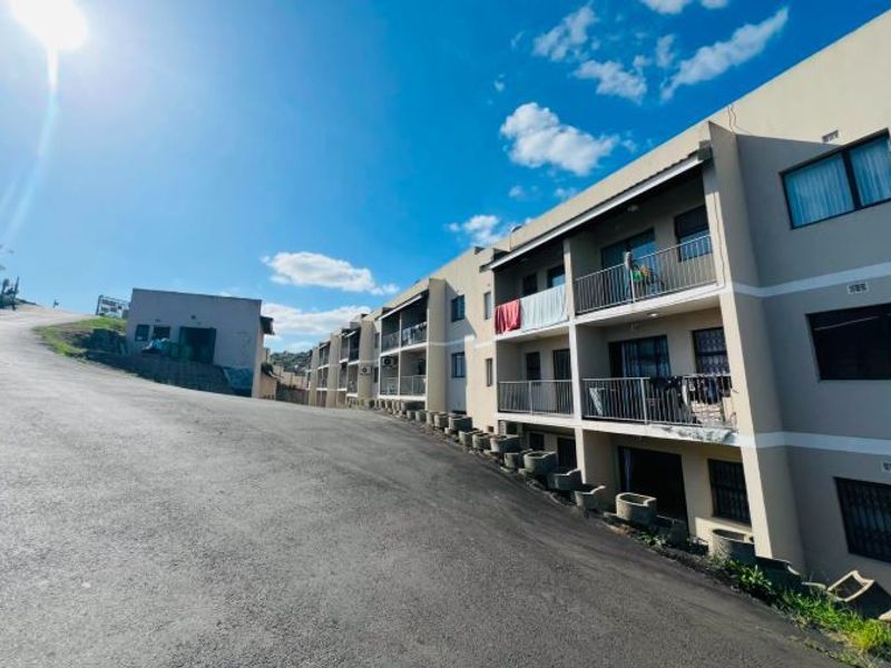 Exterior view of a multi-story apartment complex featuring private balconies with metal railings and an asphalt driveway approach.