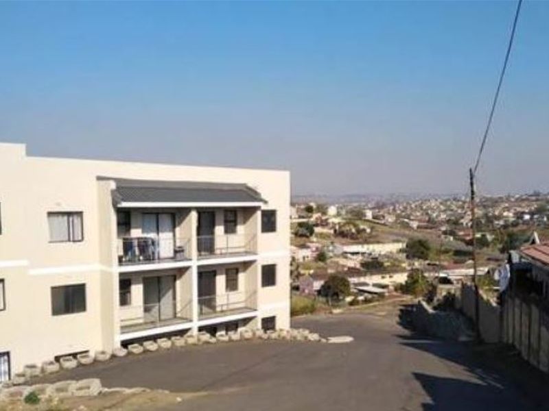Exterior view of a multi-story apartment building featuring private balconies, sliding glass doors, and an asphalt driveway with a scenic neighborhood outlook.