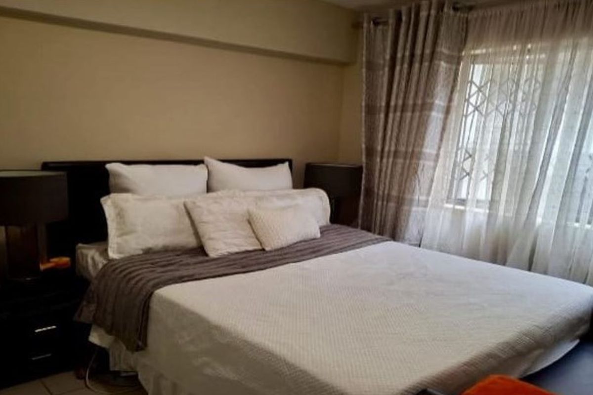 A comfortable bedroom featuring neutral wall tones, a window with security gate, and fitted curtain rails.