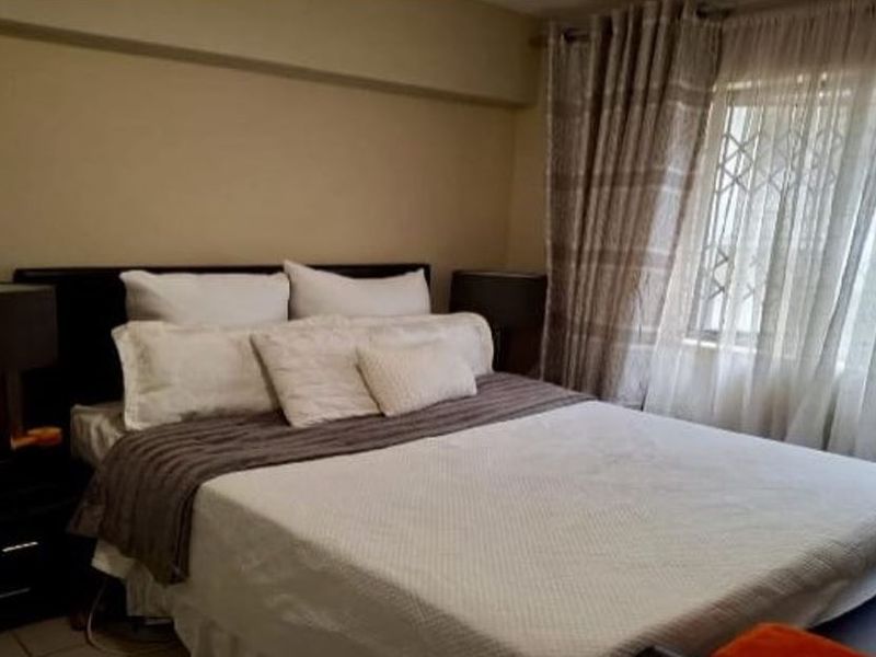 A comfortable bedroom featuring neutral wall tones, a window with security gate, and fitted curtain rails.