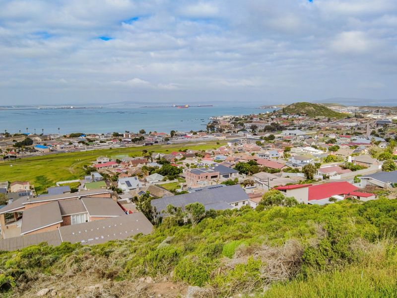 An elevated aerial view overlooking a residential coastal neighborhood with expansive ocean and bay vistas.