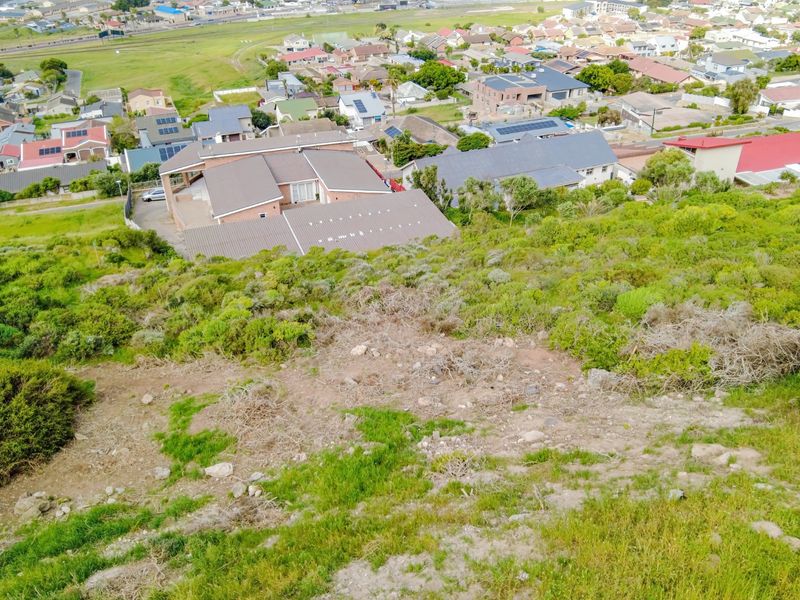 An aerial view of a sloped residential vacant land plot overlooking a suburban neighborhood.