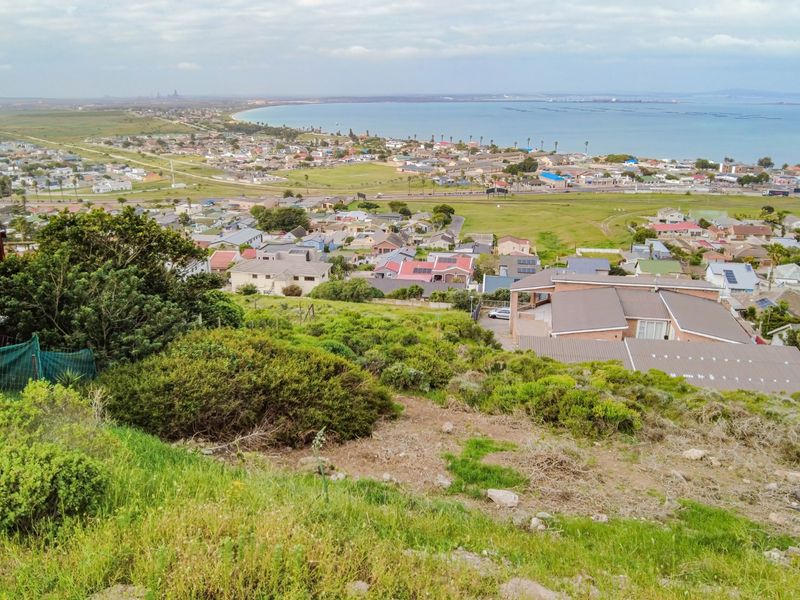 Elevated view overlooking a coastal residential neighborhood and the bay, showcasing the surrounding landscape and terrain.