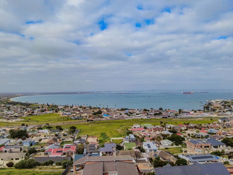 An elevated aerial view showcasing the surrounding residential neighborhood, coastal landscape, and bay area.