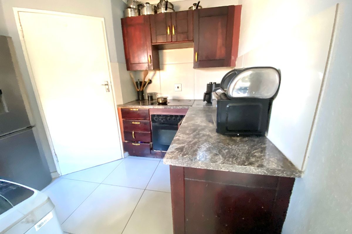 Compact kitchen featuring dark wood-finish cabinetry, stone-look laminate countertops, built-in oven, and tiled flooring.