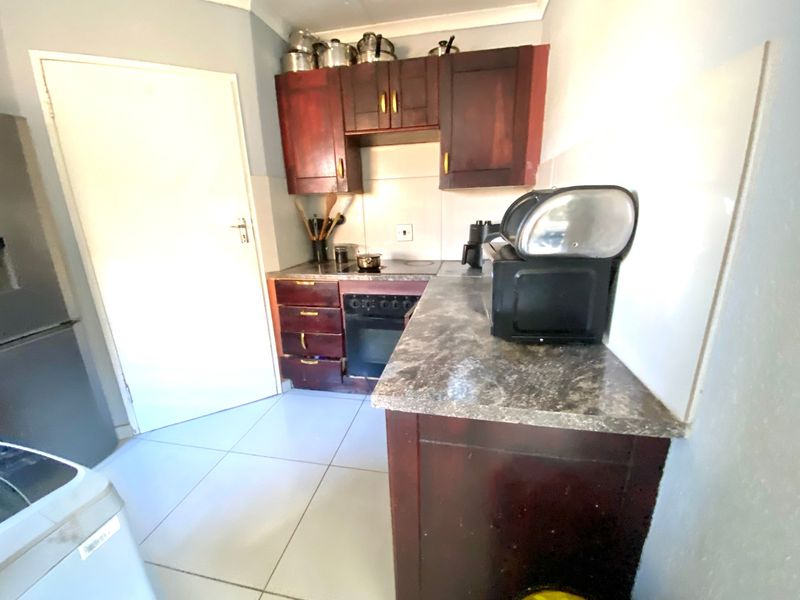 Compact kitchen featuring dark wood-finish cabinetry, stone-look laminate countertops, built-in oven, and tiled flooring.