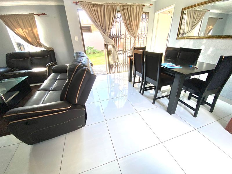 An open-plan living and dining area featuring bright tiled flooring and direct access to the rear garden through a sliding security gate.