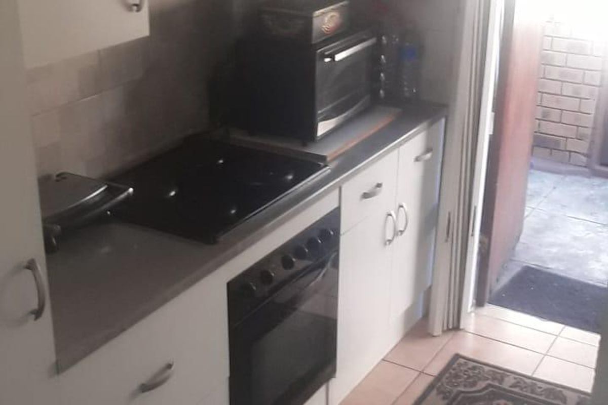 Compact kitchen featuring white cabinetry, built-in oven, electric hob, and tiled flooring with direct access to an outdoor area.