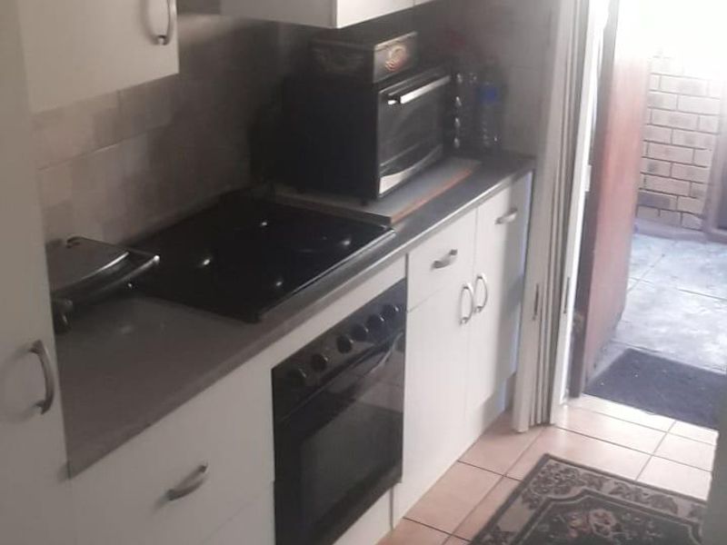 Compact kitchen featuring white cabinetry, built-in oven, electric hob, and tiled flooring with direct access to an outdoor area.