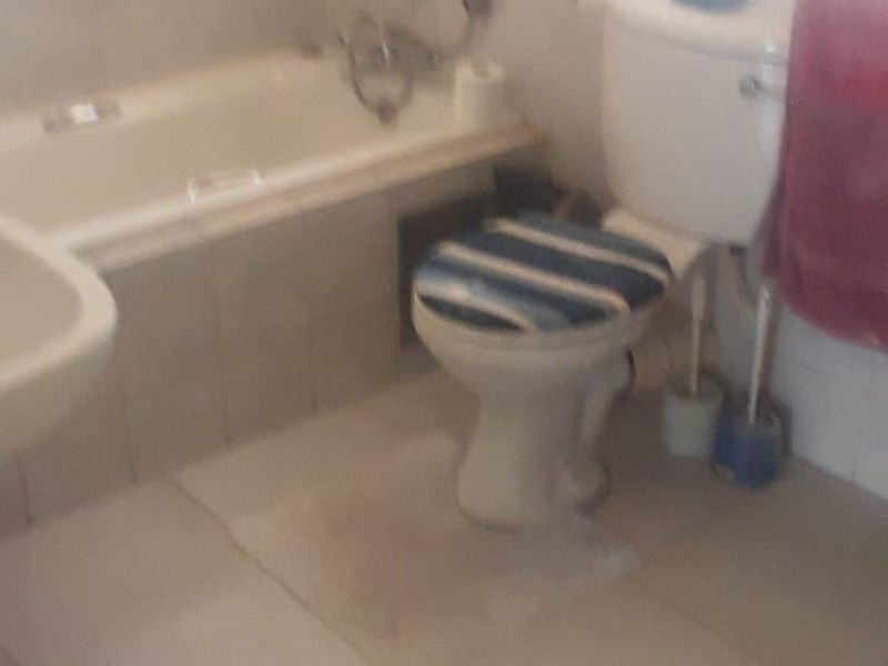 A functional bathroom featuring a bathtub, toilet, and pedestal basin with tiled finishes, requiring cosmetic updates to improve its overall condition.