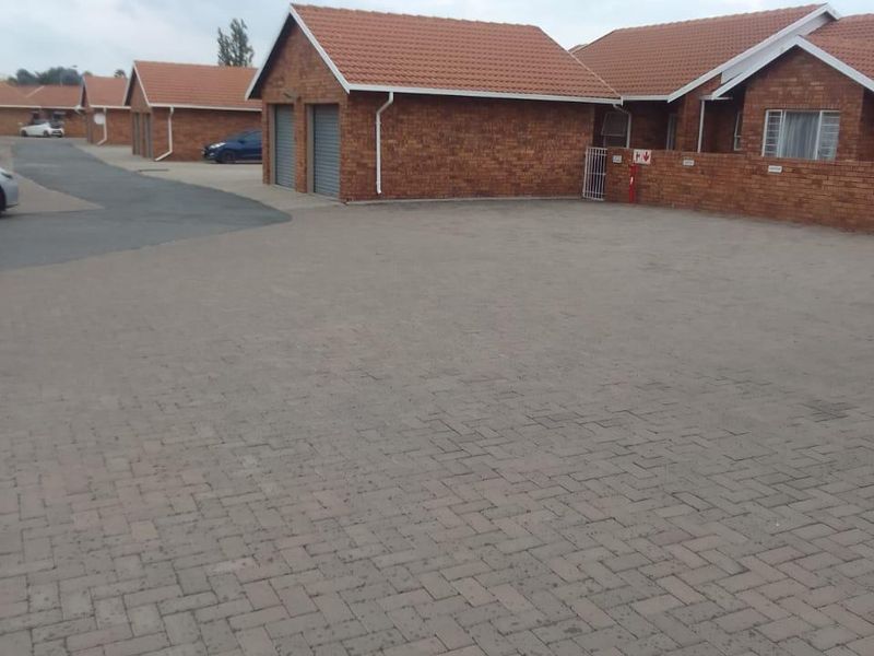 Exterior view of a townhouse complex featuring face brick construction, tiled roofs, and a paved communal driveway with garage access.