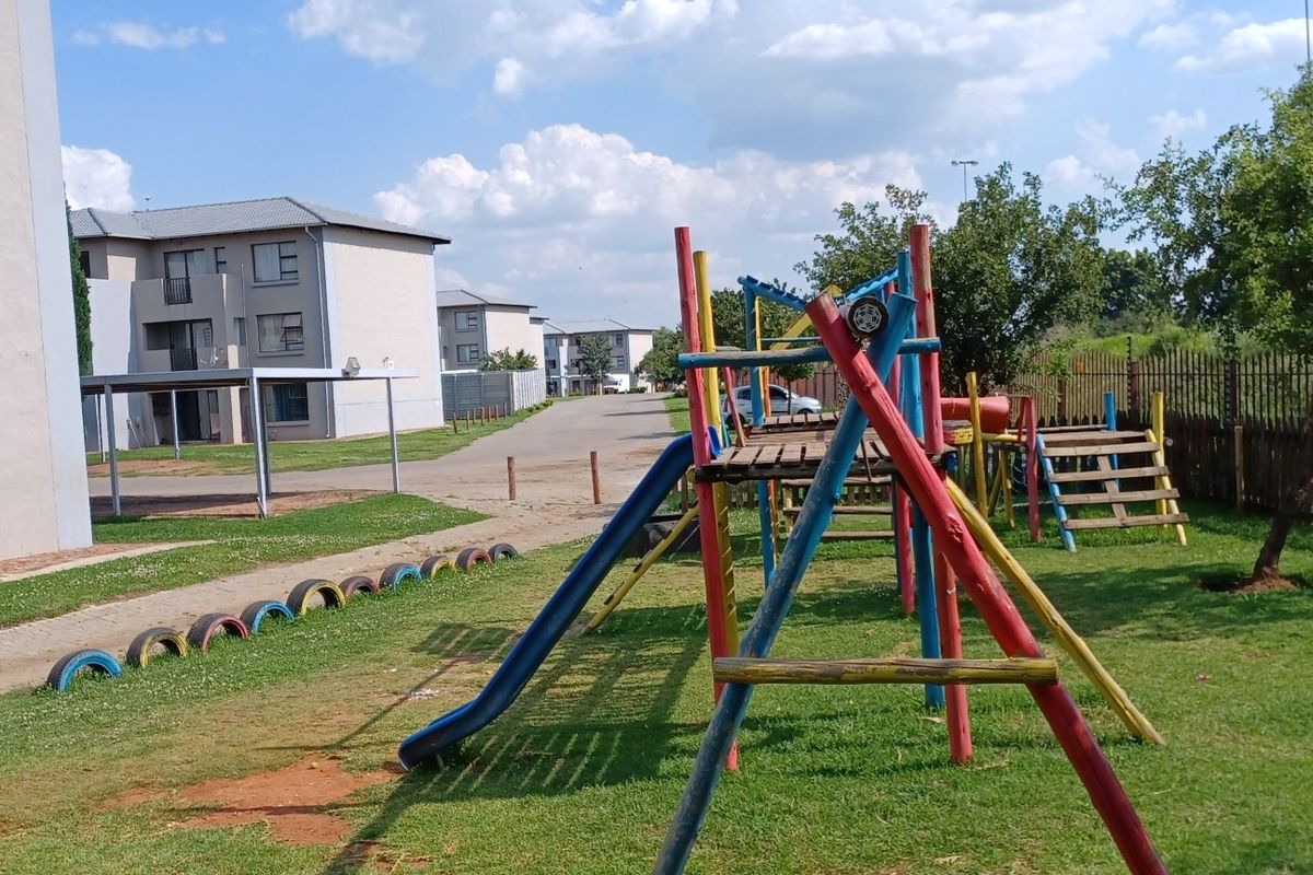 Communal outdoor area featuring a playground, lawn, and paved pathways within an apartment complex setting.