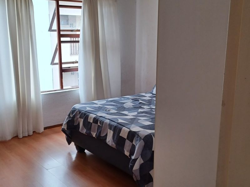 A bedroom featuring laminate flooring and a window with curtains, providing a functional living space.