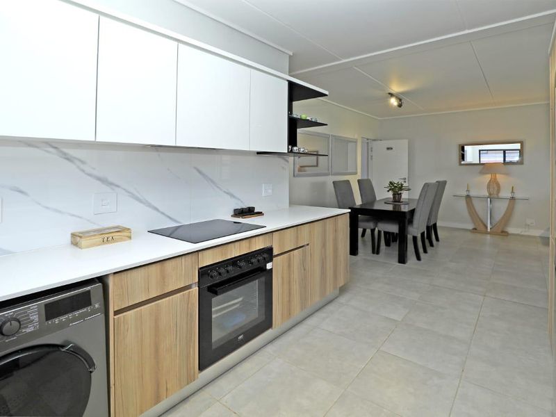 Modern open-plan kitchen and dining area featuring contemporary cabinetry, stone-look countertops, integrated appliances, and neutral tiled flooring throughout.