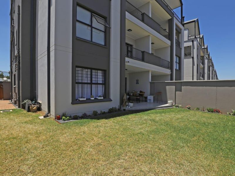 Rear view of a modern apartment building featuring a private ground floor patio, landscaped lawn, and secure boundary wall.