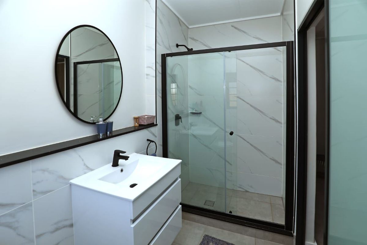 Modern bathroom featuring a sleek vanity cabinet, marble-look wall tiling, and a glass-enclosed shower with contemporary black fixtures.