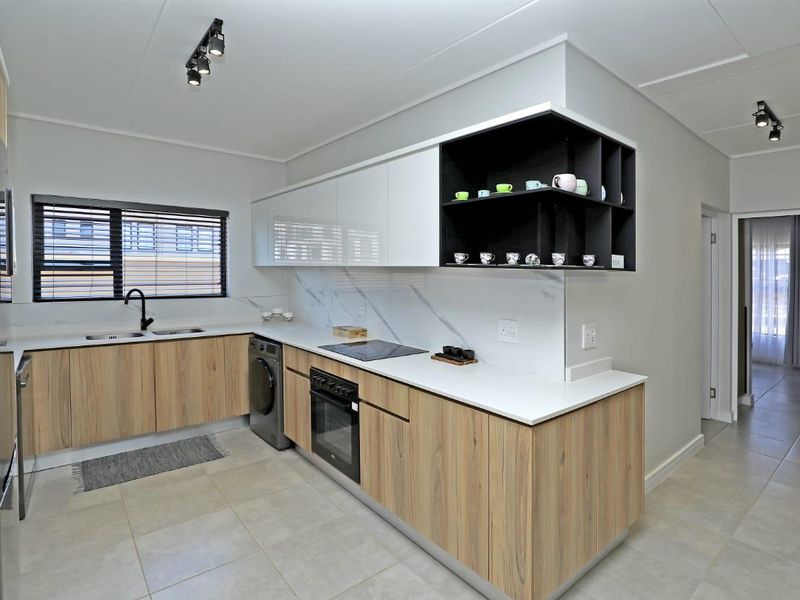 Modern kitchen featuring wood-grain cabinetry, white stone countertops, marble-look splashback, integrated oven, electric hob, and double sink with contemporary black fixtures.