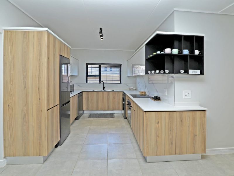 Modern kitchen featuring light wood-grain cabinetry, white stone countertops, integrated appliances, and sleek black hardware with tiled flooring.