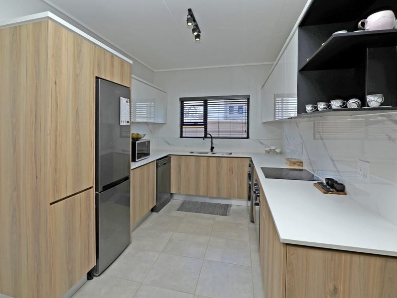 Modern kitchen featuring wood-grain and white cabinetry, stone countertops, integrated appliances, and sleek finishes with ample storage and workspace.